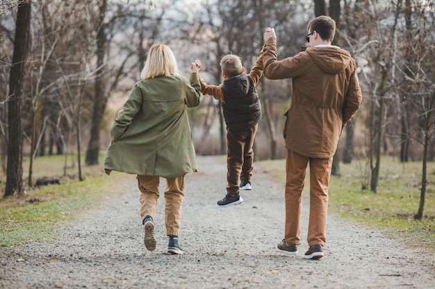 Young beautiful family walking holding hands by city park