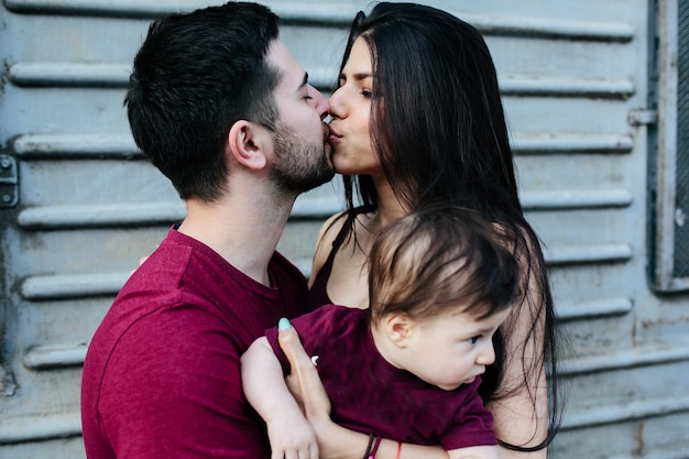 Young beautiful family with child posing on grey wall