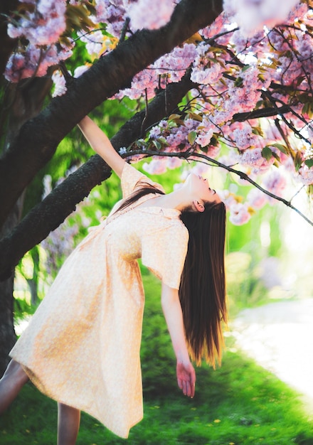 Молодая красивая модная дама позирует возле модели цветущего дерева в стильной одежде