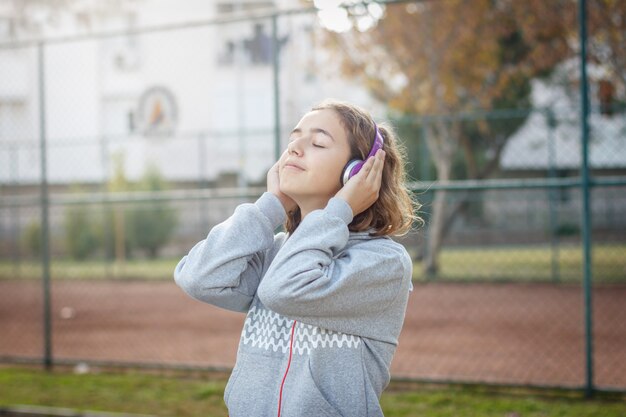 Young beautiful fashionable teenager girl listens to music on headphones from a smartphone