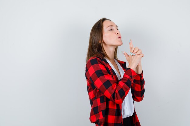 Young beautiful female blowing into the barrel of finger gun in casual outfit and looking confident , front view.