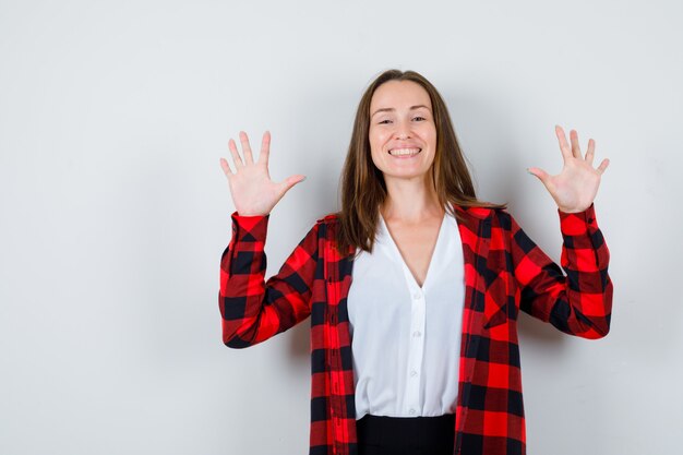 降伏のジェスチャーを示し、目をそらし、陽気に見える、カジュアルな服装の若い美しい女性、正面図。