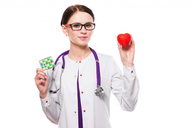 Young beautiful female doctor holding heart and pills in her hands on white background