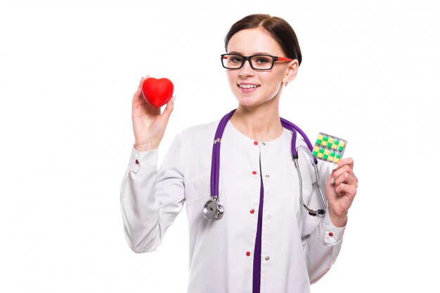 Young beautiful female doctor holding heart and pills in her hands on white background