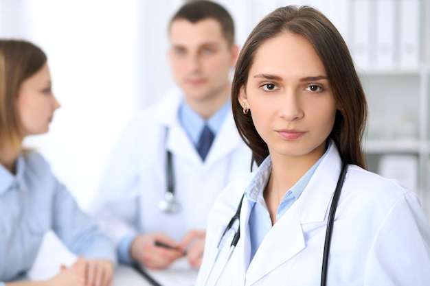 Young beautiful female doctor smiling  on the background with patient  in hospital. High level and quality medical service concept.