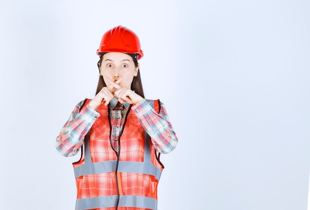 Young beautiful female engineer in helmet showing silence sign. 