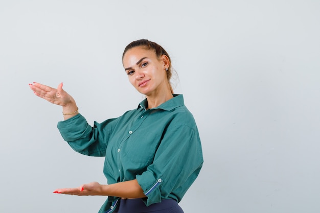 Foto giovane bella femmina in camicia verde che mostra segno di taglia e sembra gioiosa, vista frontale.