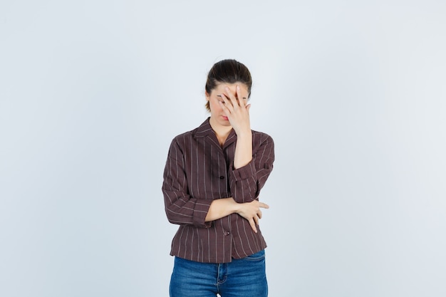 Young beautiful female keeping hand on face in jacket and looking disappointed. front view.