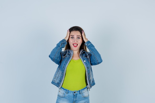 Giovane bella donna che tiene le mani sulla testa in abito di jeans e sembra turbata. vista frontale.