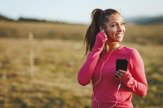 Young beautiful female runner listening to music and preparing to jogging at morning in mountains.