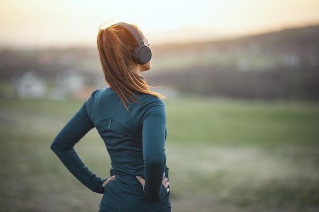 Giovane bella corridore femminile che ascolta musica e si prepara a fare jogging in montagna. retrovisore.