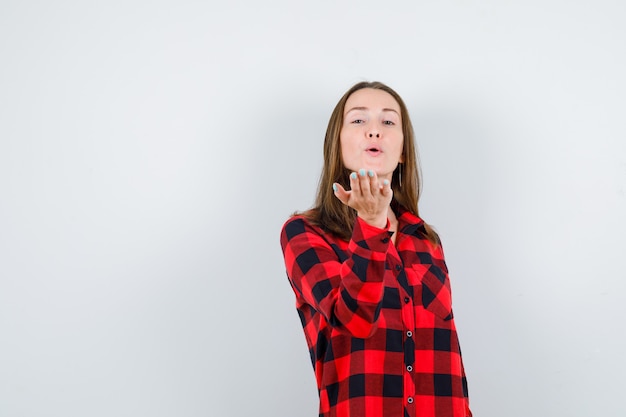 Photo young beautiful female sending air kiss with pouted lips in casual shirt and looking confident , front view.