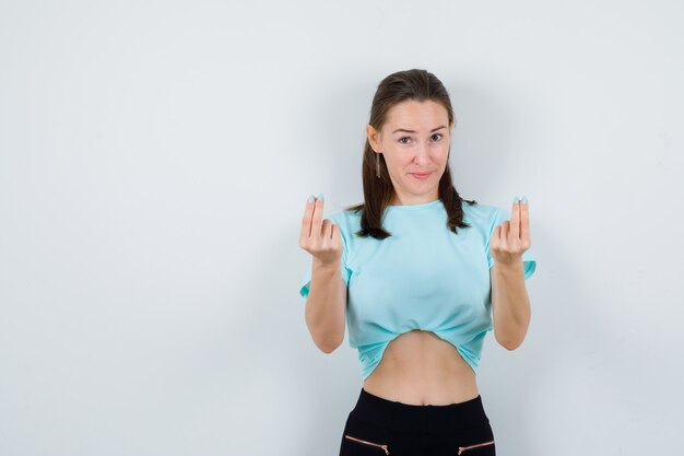 Young beautiful female showing money gesture in t-shirt and looking joyful , front view.