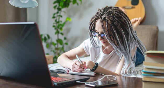 Una giovane e bella studentessa con i dreadlocks sta studiando in una lezione online a casa in una stanza con un laptop