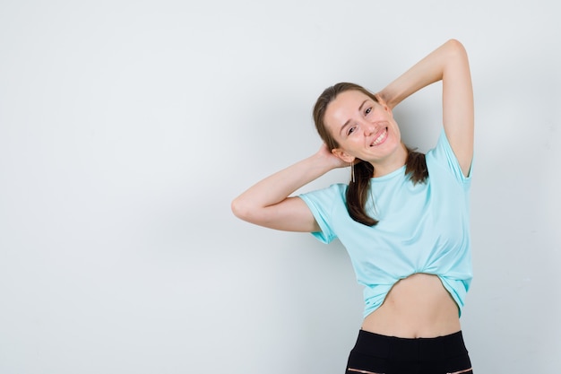 Young beautiful female in t-shirt posing with hands behind head and looking joyful , front view.