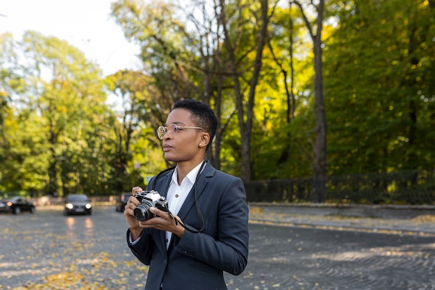 アナログフィルムカメラで公園で写真を撮る若い美しい女性の観光写真家