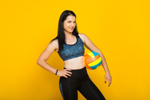 Young beautiful female volleyball player isolated on yellow