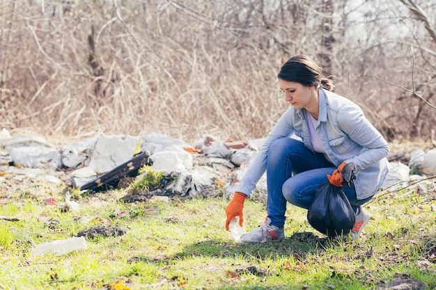 Young beautiful female volunteer collects plastic garbage in the forest 