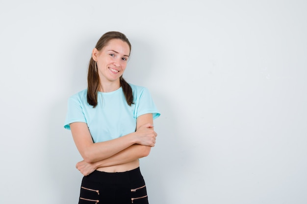 Young beautiful female with arms folded in t-shirt, pants and looking blissful , front view.