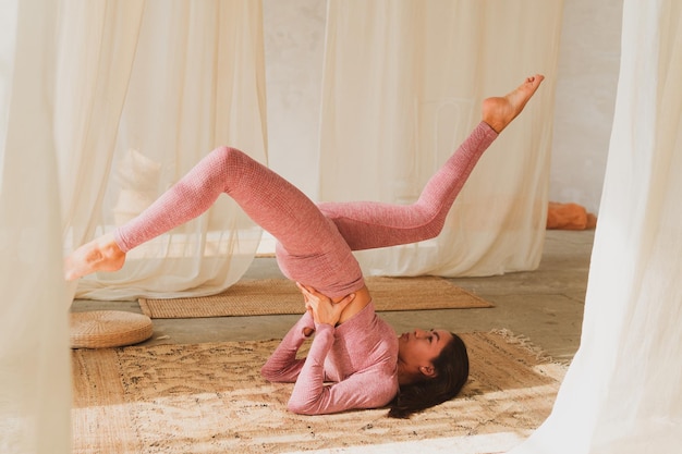 Young beautiful flexible girl doing yoga pose stretching in a cozy sunny room