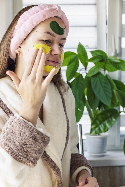 Young beautiful fun girl applying treatment facial mask self\
care and personal hygiene