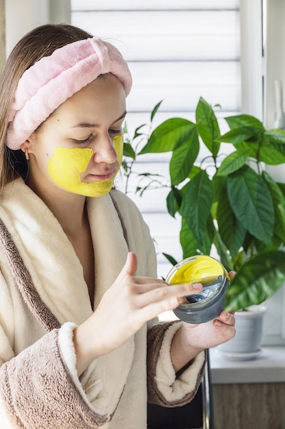 Young beautiful fun girl applying treatment facial mask Self care and personal hygiene