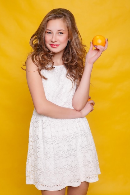 사진 주황색 배경에 주황색 조각이 있는 젊고 아름다운 재미있는 패션 모델. 메이크업과 헤어스타일로. 좋은 미소로 레몬을 들고입니다.