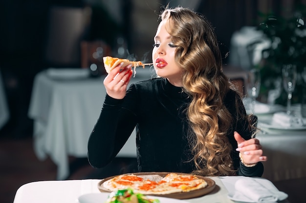 Young beautiful girl alone eating pizza in a restaurant.