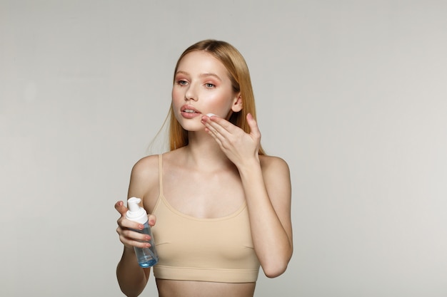 Young beautiful girl applying cosmetic cream on face