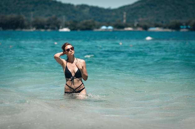 A young beautiful girl in black sunglasses and black bikini staying in blue water in the sea ,enjoying beach holiday