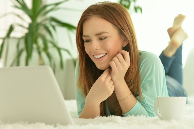 Young beautiful girl communicating via laptop lying on bed