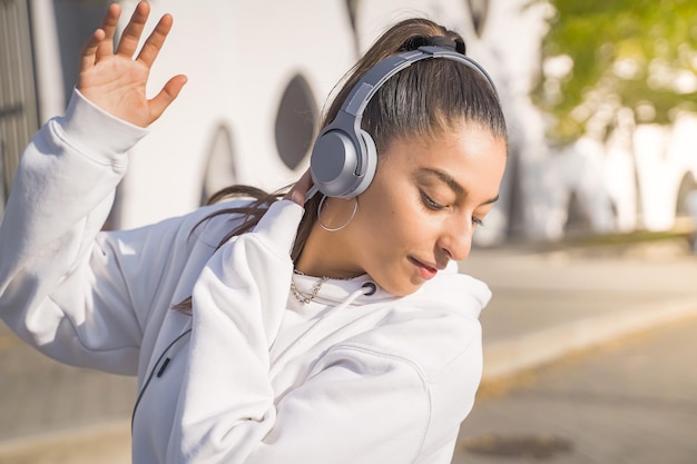 ヘッドフォンで通りで幸せに踊る若い美しい少女