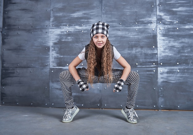 Young beautiful girl dancing in a trendy clothes on a grunge wall