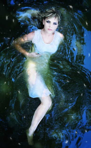 Young beautiful girl in a dark river water, top view