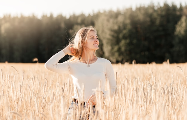 A young beautiful girl in a denim skirt walks through a wheat field on a sunny day