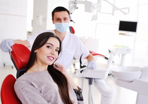 Young beautiful girl in dental chair and dentist smiling at camera