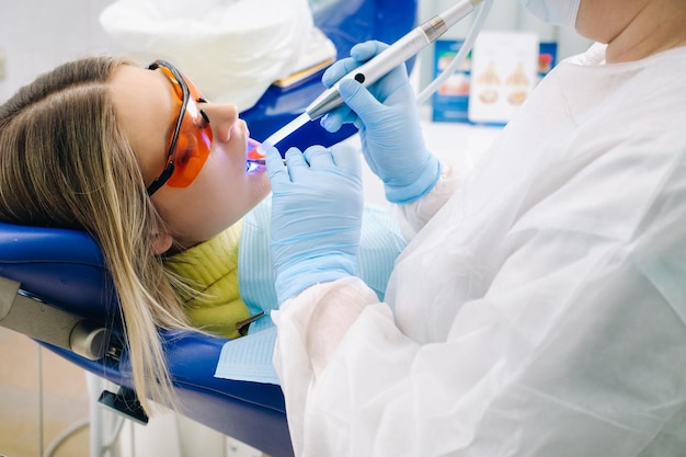 A young beautiful girl in dental glasses treats her teeth at the dentist with ultraviolet light filling of teeth