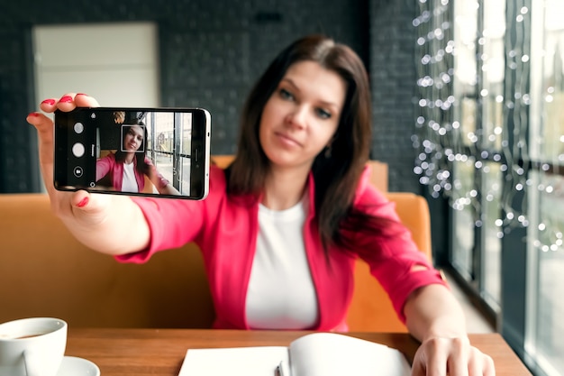 Young beautiful girl doing selfie sitting in cafe.