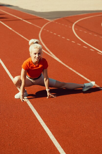 学校のスタジアムでスポーツ運動の前にウォームアップをしている若い美しい少女