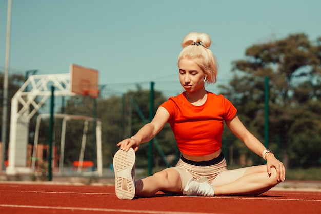 Young beautiful girl doing warm-up before sports exercise at school stadium