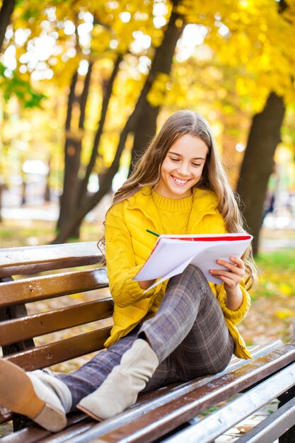 Young beautiful girl draws with a pencil in the sketchbook while sitting in the autumn park