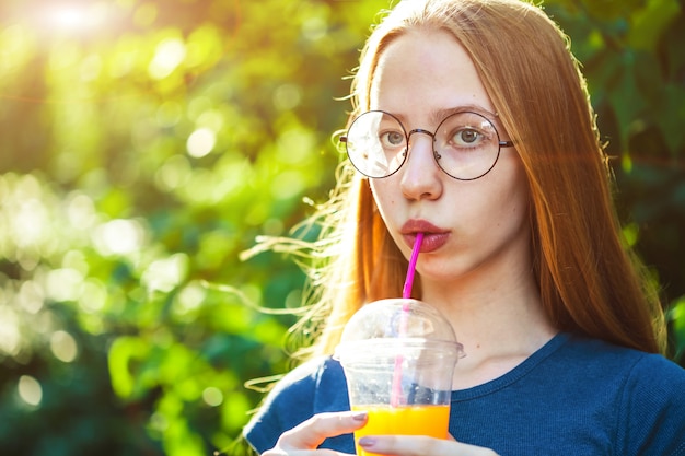 美しい少女は、背景に絞りたてのジュースを飲みます。