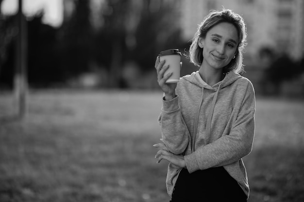 Young beautiful girl drinks lat from a paper cup on the street black and white photo