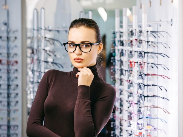 Young beautiful girl in glasses near the stand in the optical store.