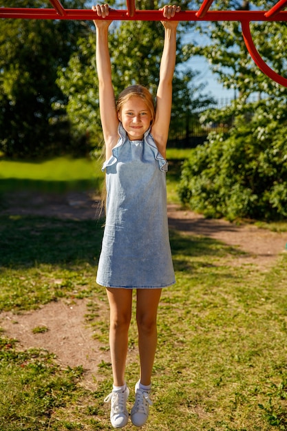 Young beautiful girl hanging on the horizontal bar in the park