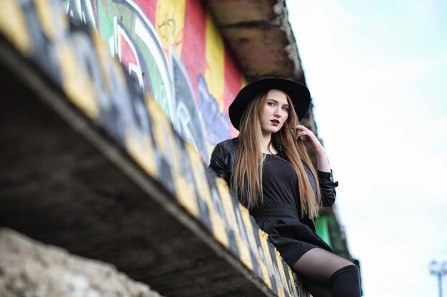 Young beautiful girl in a hat and with a dark make-up outside. Girl in the Gothic style on the street. A girl walks down the city street in a leather waistcoat with phone.