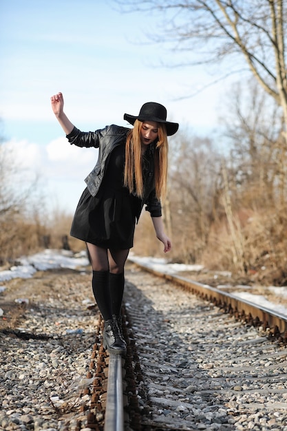 Young beautiful girl in a hat and with a dark make-up outside. Girl in the Gothic style on the street. A girl walks down the city street in a leather waistcoat with phone.