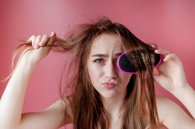 Young beautiful girl having problems while hair on pink wall