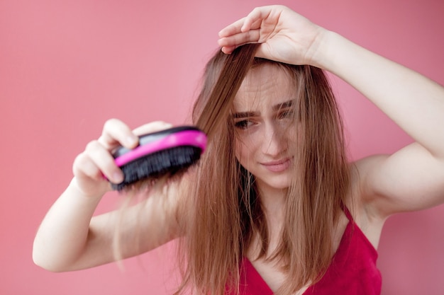 Giovane bella ragazza che ha problemi mentre capelli sulla parete rosa