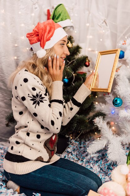 young beautiful girl holding a mirror sitting near the Christmas tree in a sweater